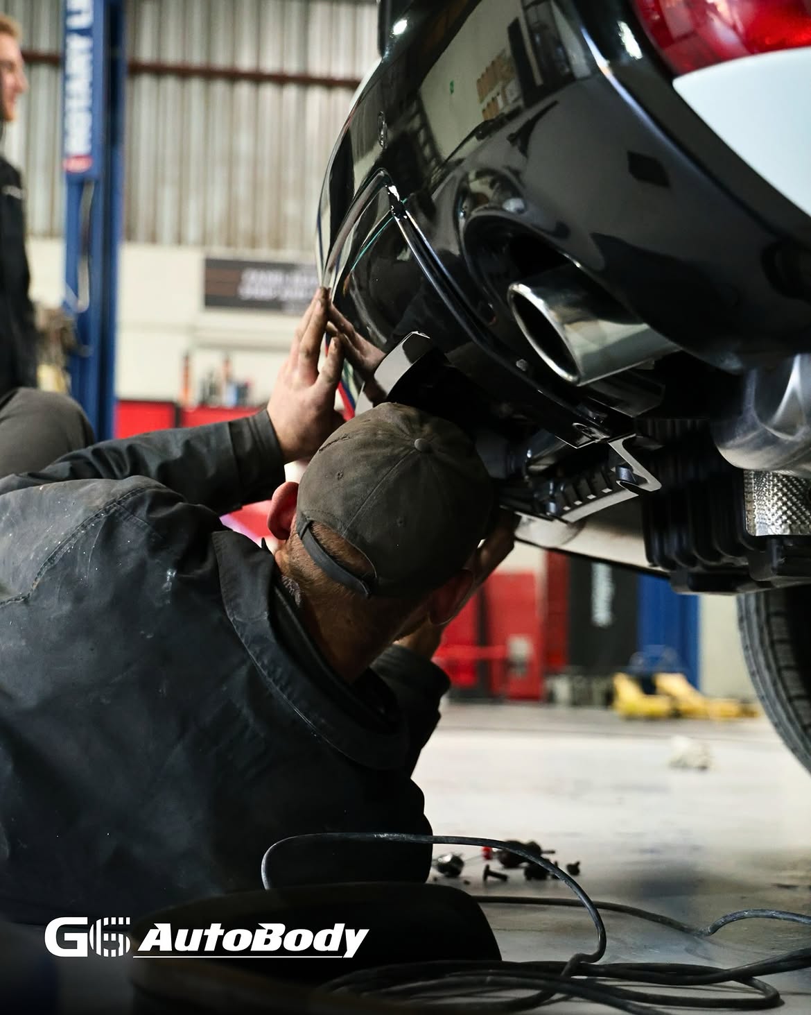 G6 AutoBody technicians precision-fitting a rear bumper on a lifted vehicle