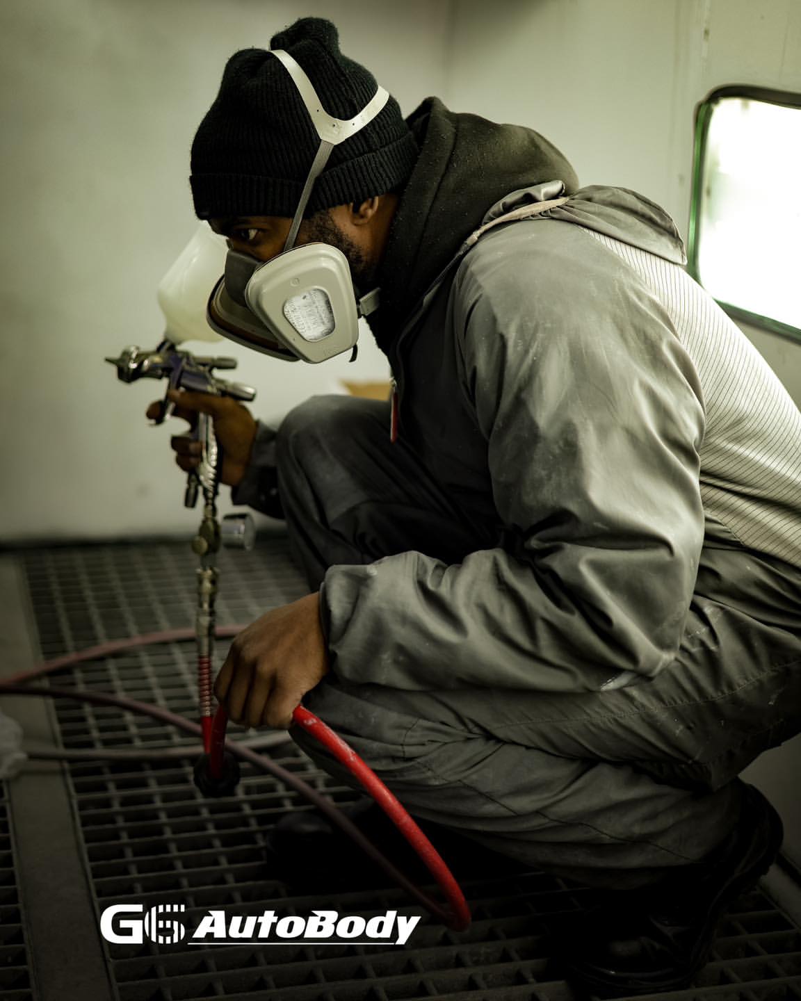 G6 AutoBody painter crouched in the spray booth applying colour to a panel
